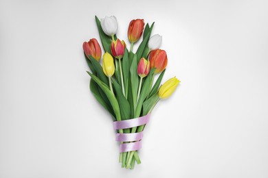 Bouquet of beautiful colorful tulip flowers tied with pink ribbon on white background, top view