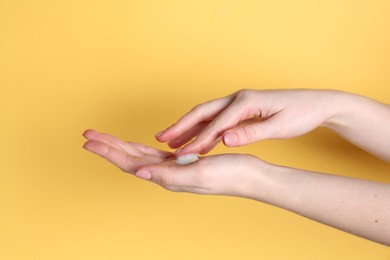 Woman applying cream on her hand against yellow background, closeup