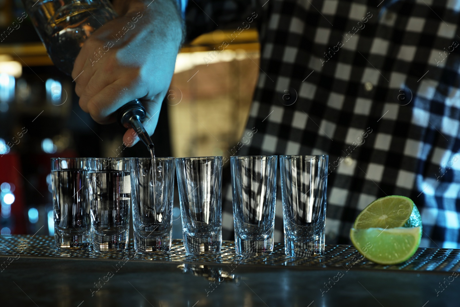 Photo of Bartender pouring Mexican Tequila into shot glasses at bar counter, closeup