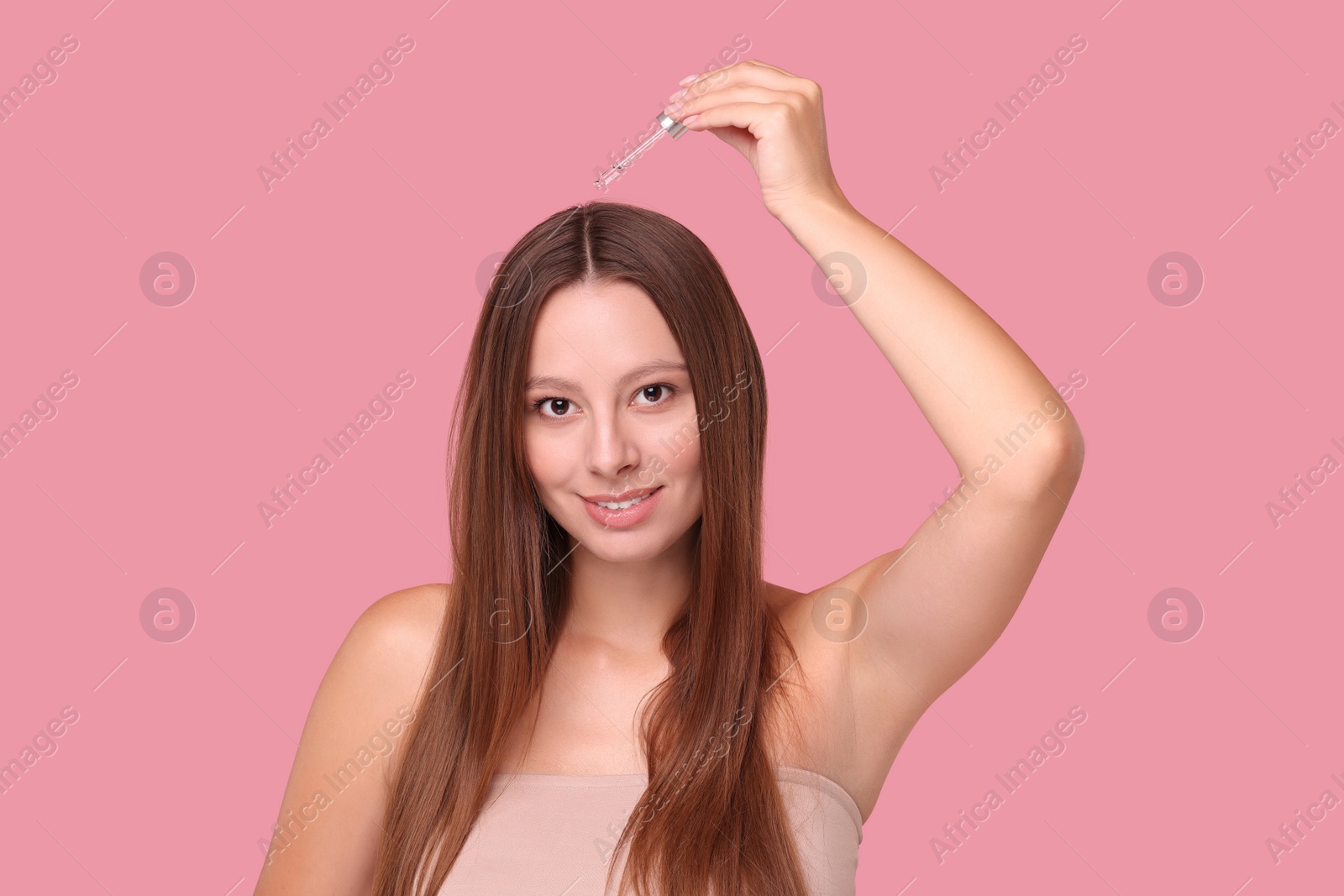 Photo of Beautiful woman applying serum onto hair on pink background