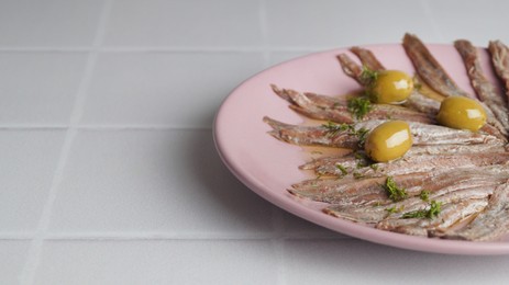 Photo of Canned anchovy fillets with olives on white tiled table, space for text