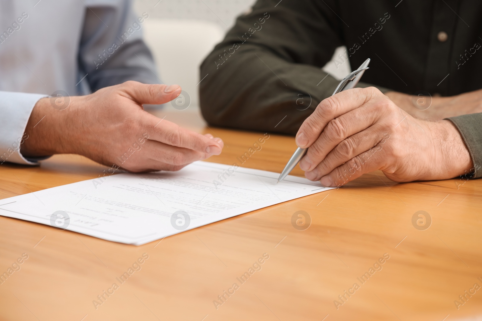 Photo of Notary showing senior man where to sign Last Will and Testament at wooden table indoors, closeup