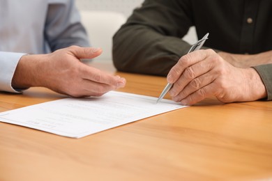 Photo of Notary showing senior man where to sign Last Will and Testament at wooden table indoors, closeup