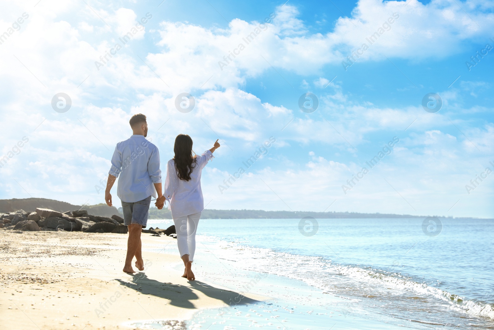 Photo of Young couple walking on beach near sea, back view. Honeymoon trip