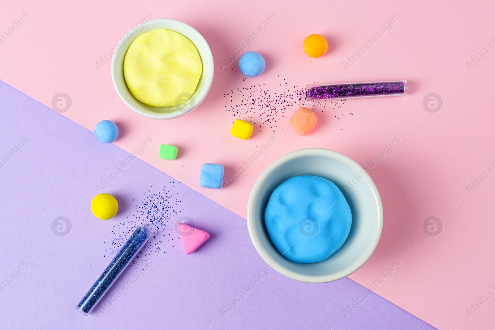 Photo of Bowls with bright play dough and shiny glitter on color background, flat lay