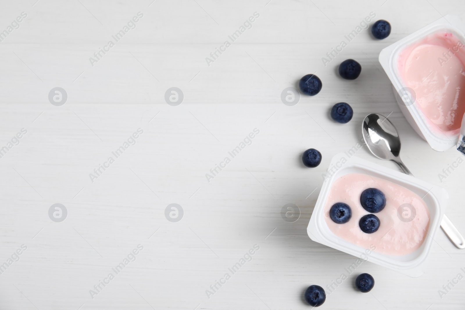Photo of Plastic cups with tasty yogurts and blueberries on white wooden table, flat lay. Space for text