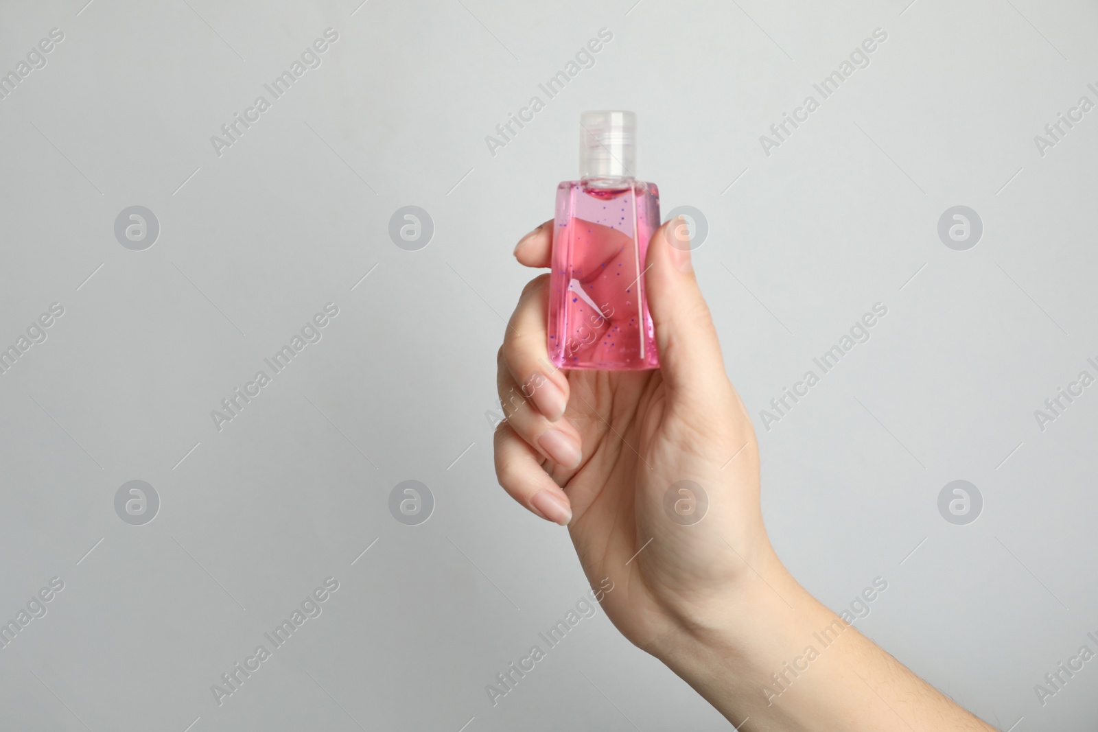 Photo of Woman holding antiseptic gel on light grey background, closeup