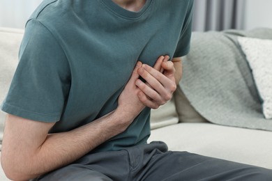 Man suffering from heart hurt on sofa at home, closeup