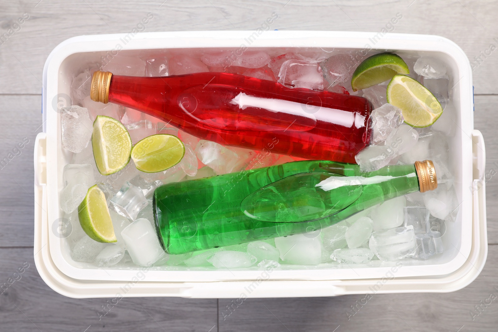 Photo of Plastic cool box filled ice cubes, lime and refreshing drinks on wooden floor, top view