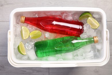 Photo of Plastic cool box filled ice cubes, lime and refreshing drinks on wooden floor, top view