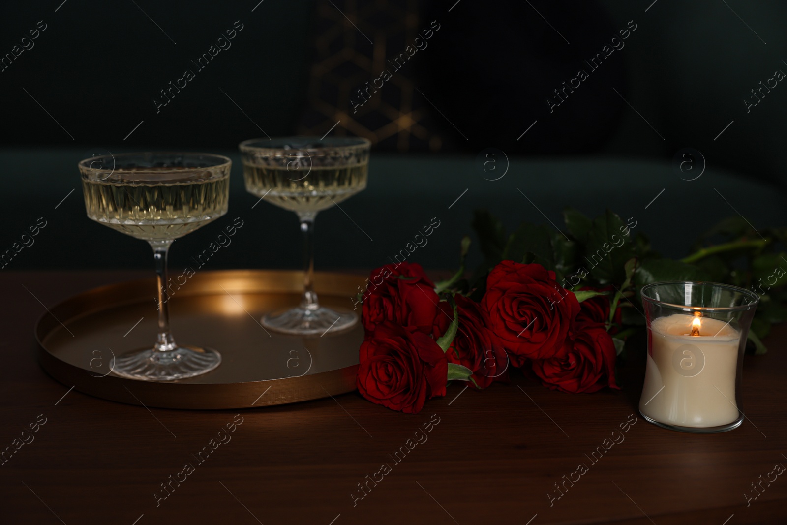 Photo of Burning candle, glasses of wine and beautiful red roses on wooden table indoors