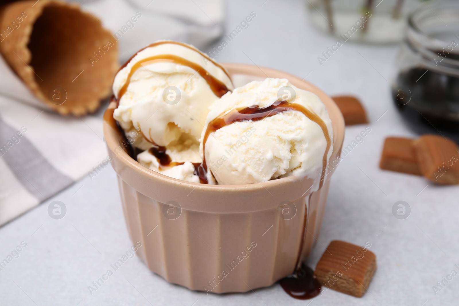 Photo of Scoops of ice cream with caramel sauce and candies on light grey table, closeup