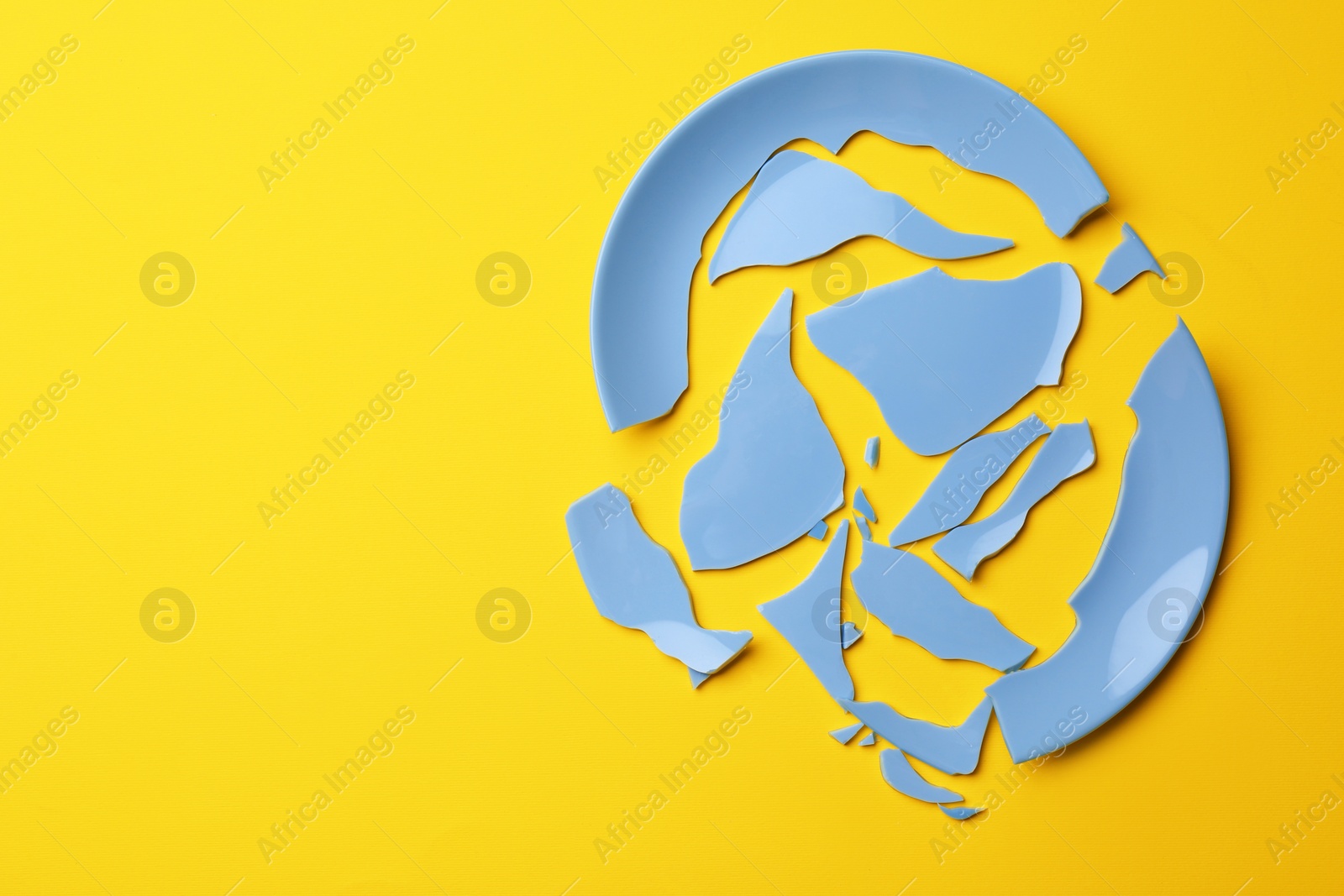 Photo of Pieces of broken light blue ceramic plate on yellow background, top view. Space for text