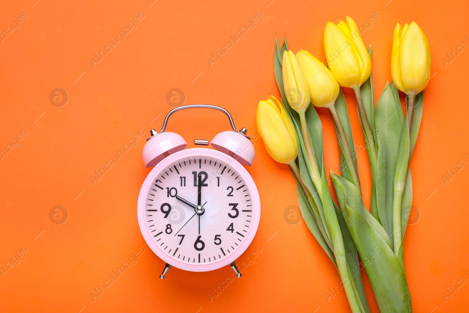 Photo of Pink alarm clock and beautiful tulips on orange background, flat lay. Spring time