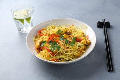 Photo of Stir-fry. Delicious cooked noodles with chicken and vegetables in bowl served on gray textured table