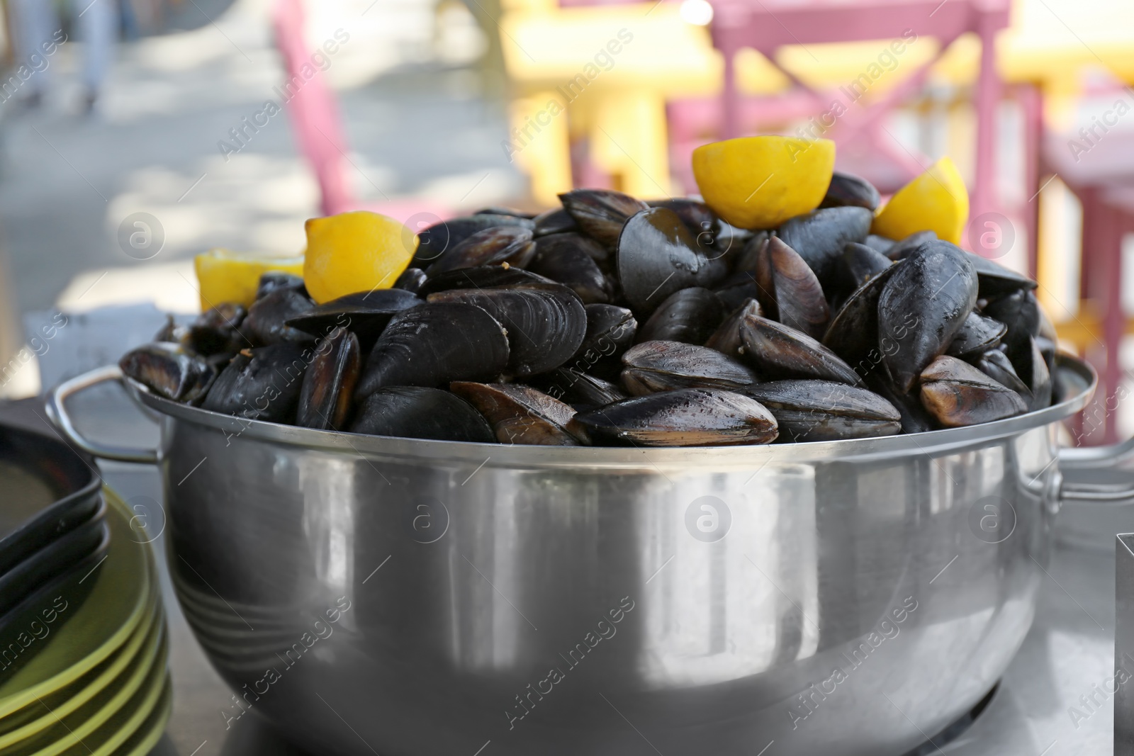 Photo of Stewpan with fresh mussels and lemons on table, closeup