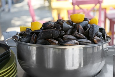 Stewpan with fresh mussels and lemons on table, closeup