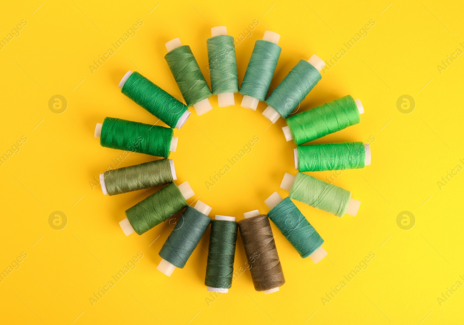 Photo of Different shades of green sewing threads on yellow background, flat lay. Space for text