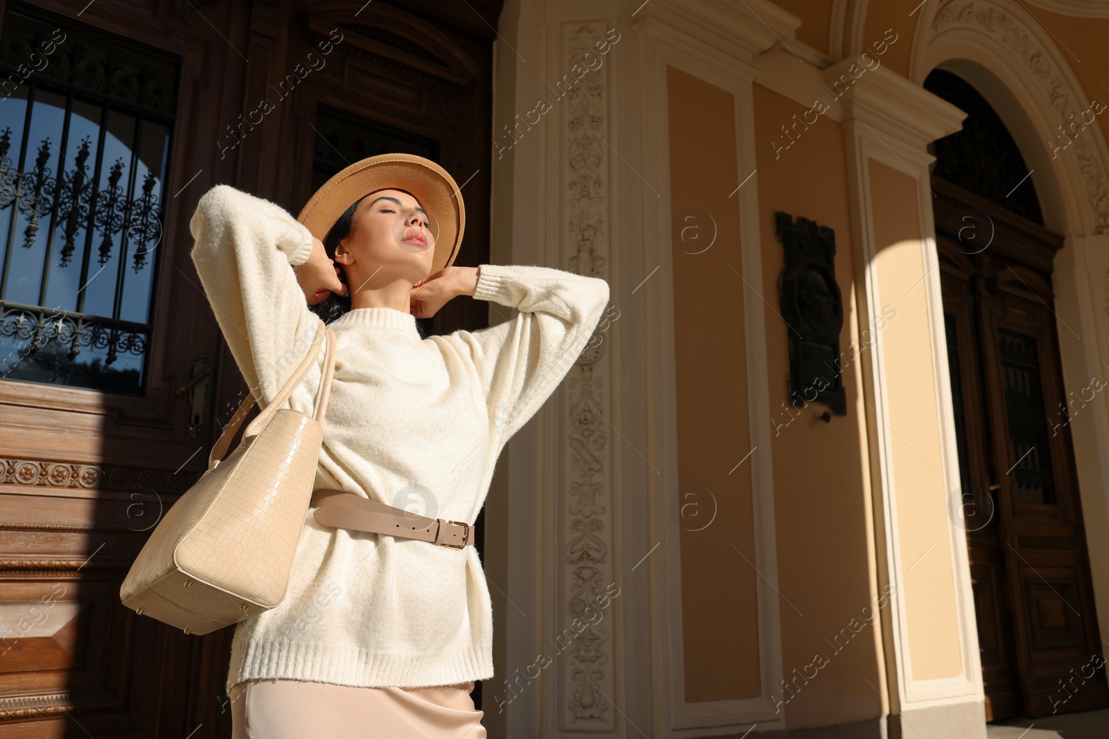 Photo of Young woman with stylish bag outside beautiful building, low angle view. Space for text