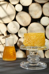 Photo of Glass stand with natural honeycomb and honey on black table, selective focus. Space for text