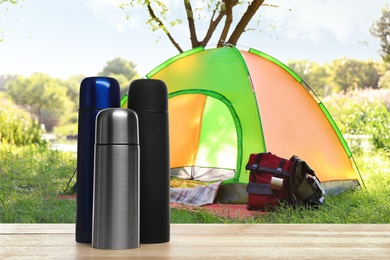 Image of Modern thermo bottles outdoors, space for text. Camping season 