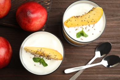Photo of Tasty peach dessert with yogurt and chia seeds served on wooden table, flat lay