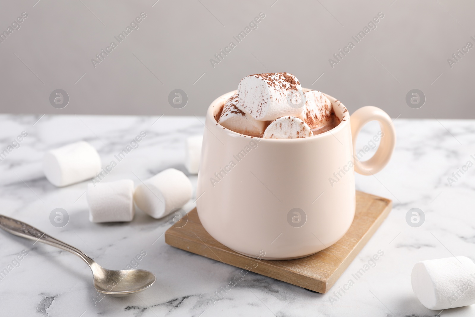 Photo of Cup of aromatic hot chocolate with marshmallows and cocoa powder served on white marble table