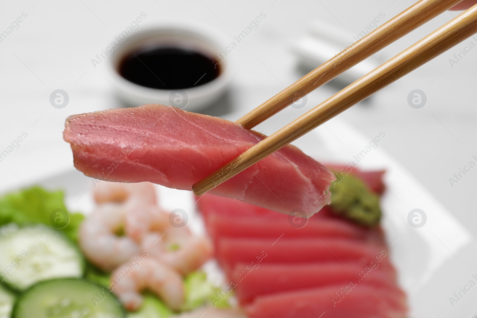 Photo of Chopsticks with tasty sashimi (piece of fresh raw tuna) against blurred background, closeup
