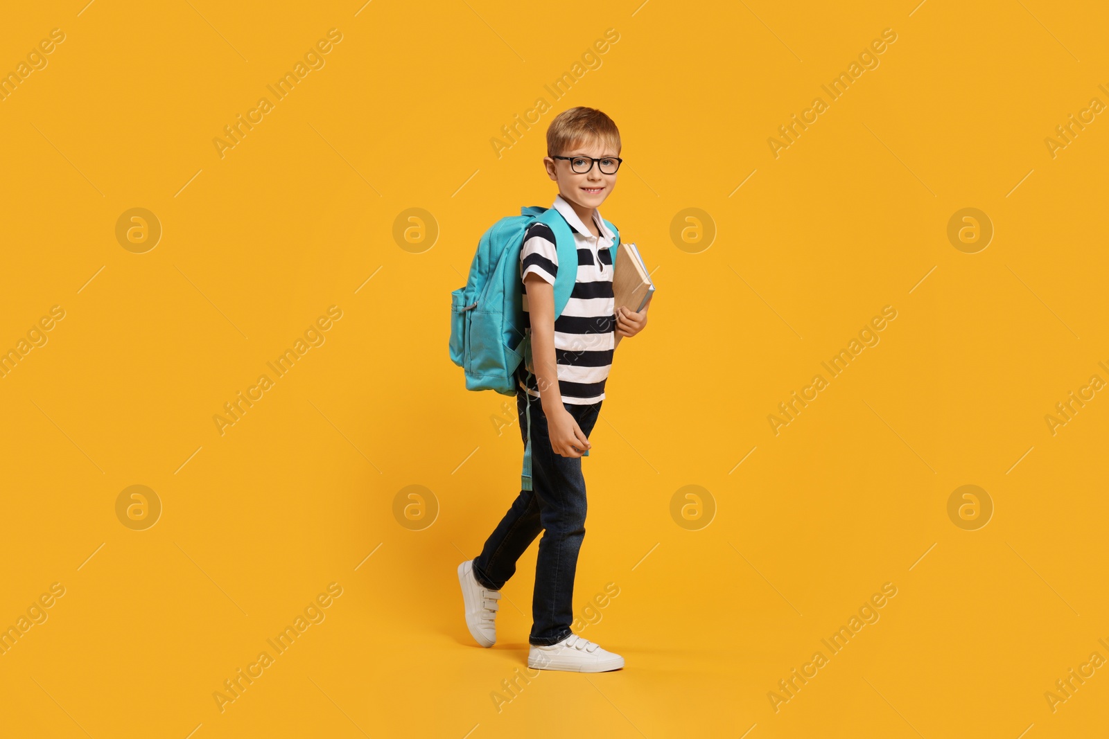 Photo of Happy schoolboy in glasses with backpack and books on orange background