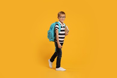 Happy schoolboy in glasses with backpack and books on orange background