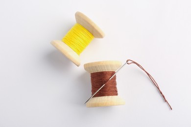 Colorful sewing threads with needle on white background, top view