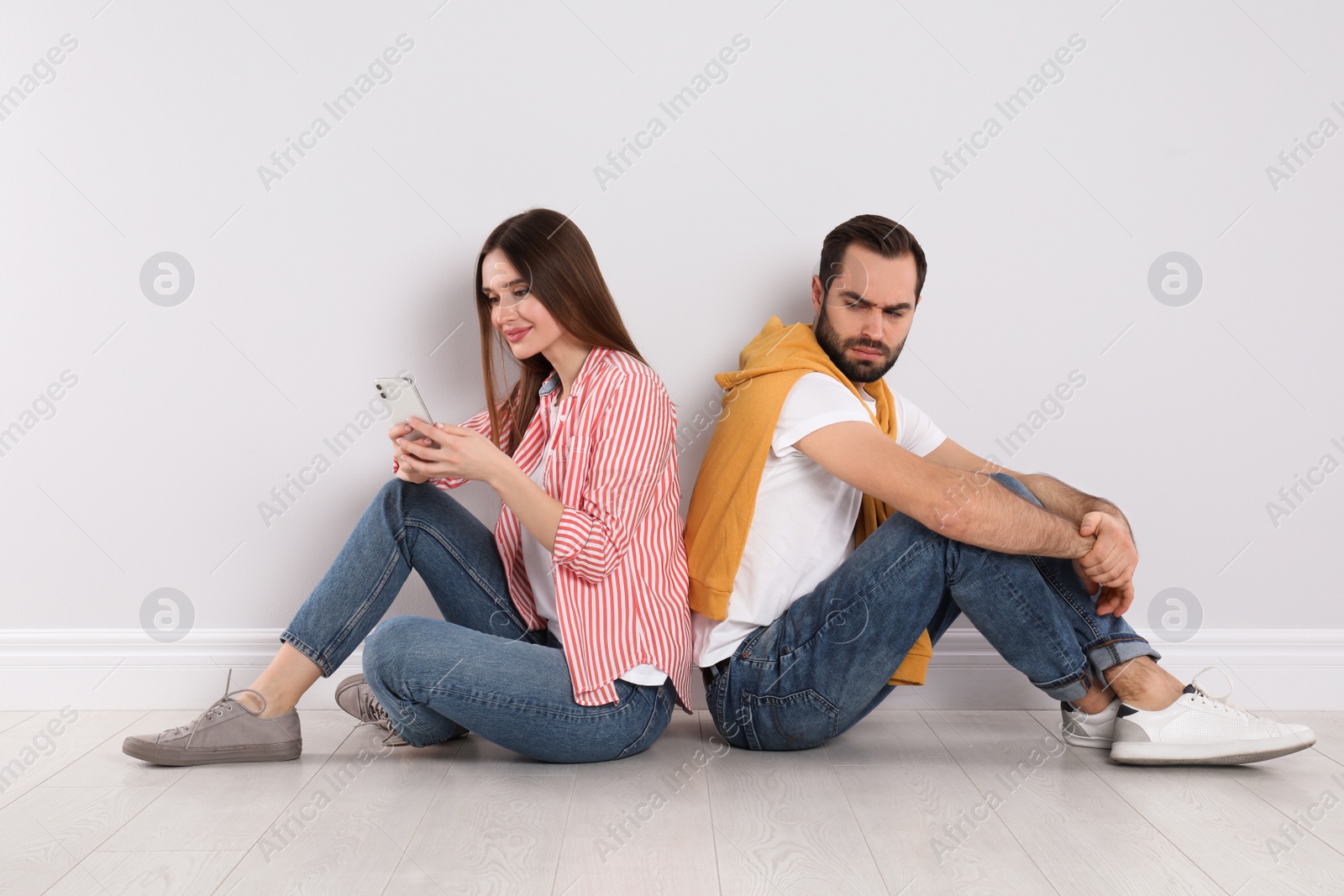 Photo of Distrustful young man peering into girlfriend's smartphone indoors. Relationship problems