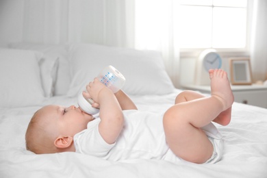 Baby drinking milk from bottle on bed at home