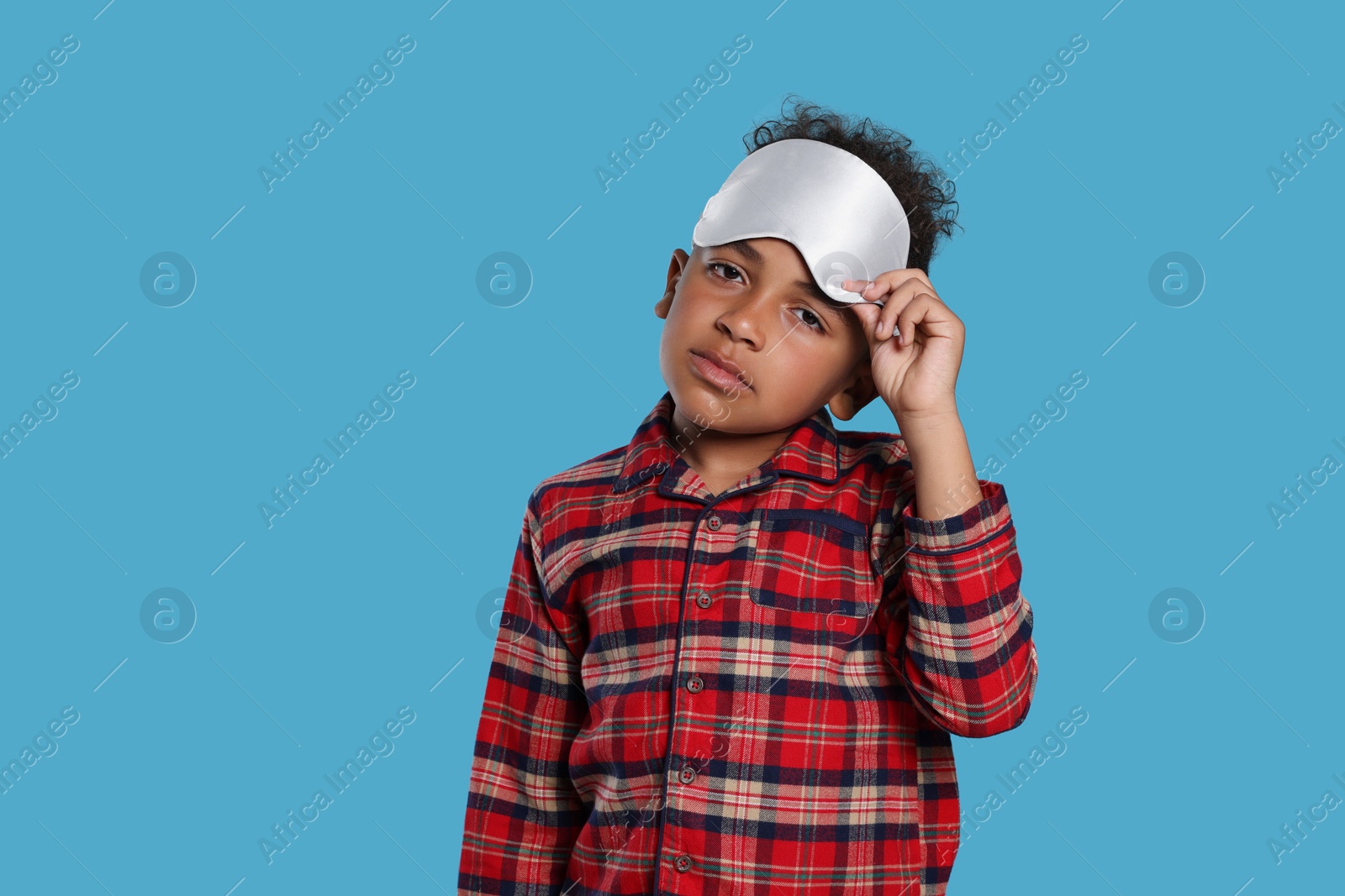 Photo of Boy with sleep mask on light blue background. Insomnia problem