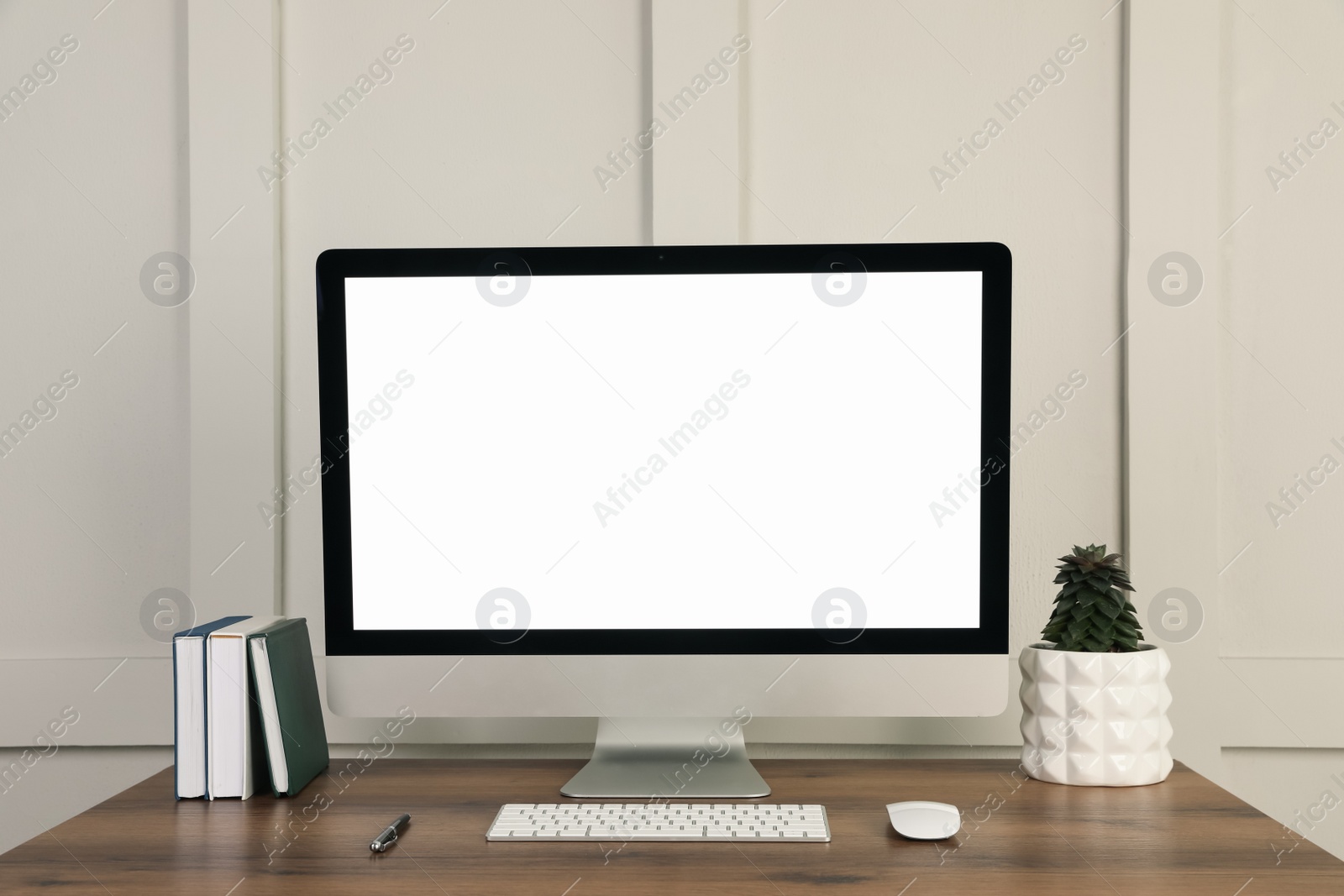 Photo of Modern computer, notebooks, pen and houseplant on wooden table near molding wall