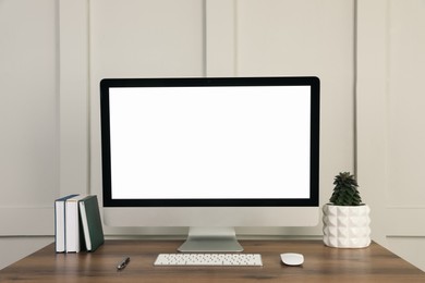 Modern computer, notebooks, pen and houseplant on wooden table near molding wall