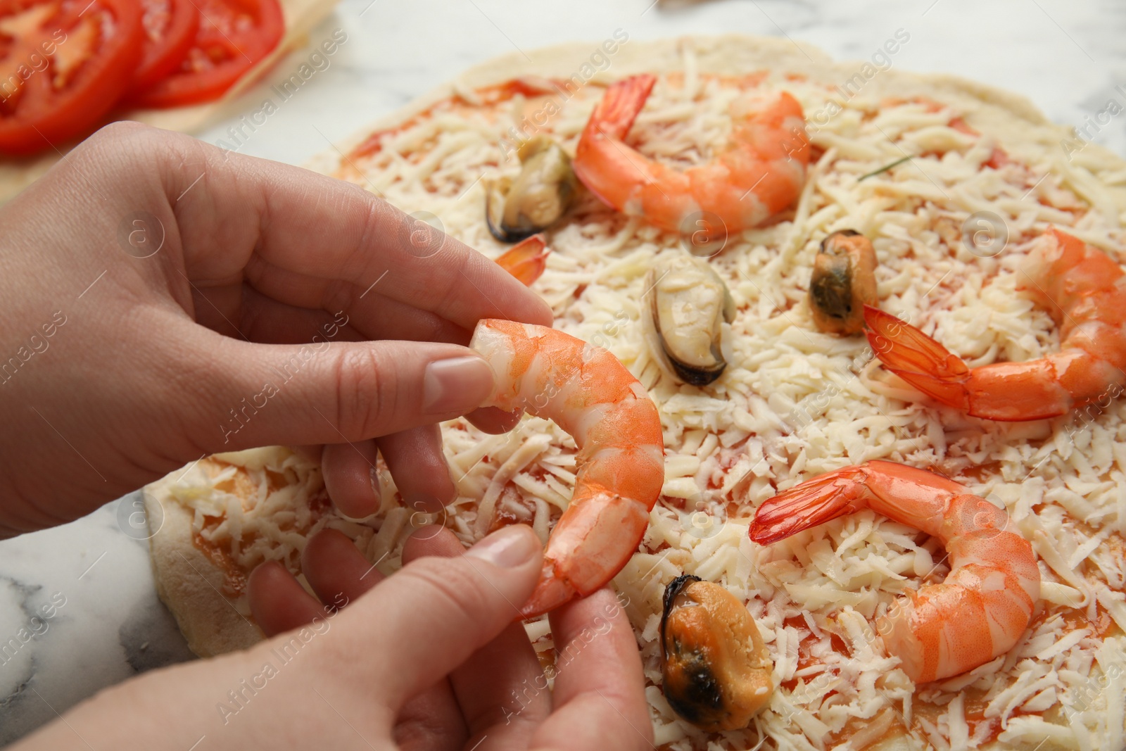 Photo of Woman adding shrimp to seafood pizza at white marble table, closeup