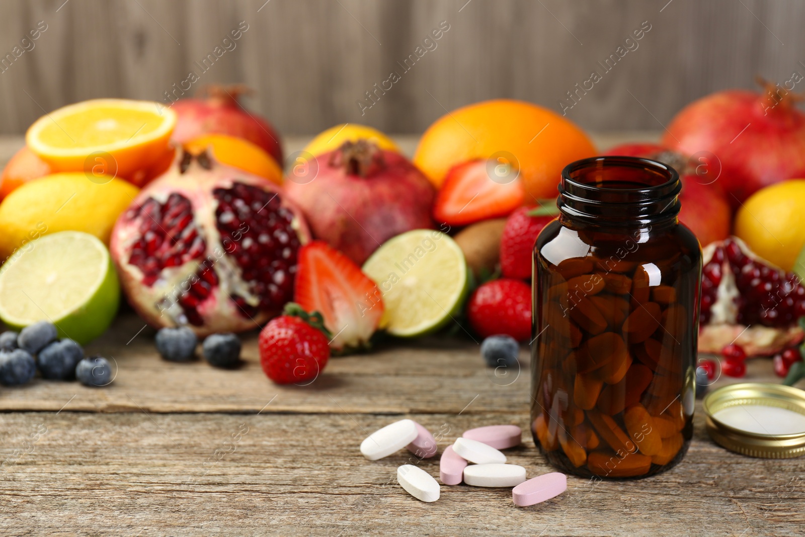 Photo of Vitamin pills, bottle and fresh fruits on wooden table. Space for text