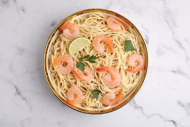 Tasty spaghetti with shrimps, lime and parsley in bowl on white marble table, top view