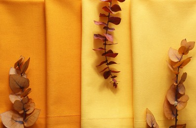 Photo of Different kitchen napkins and decorative dry leaves as background, top view