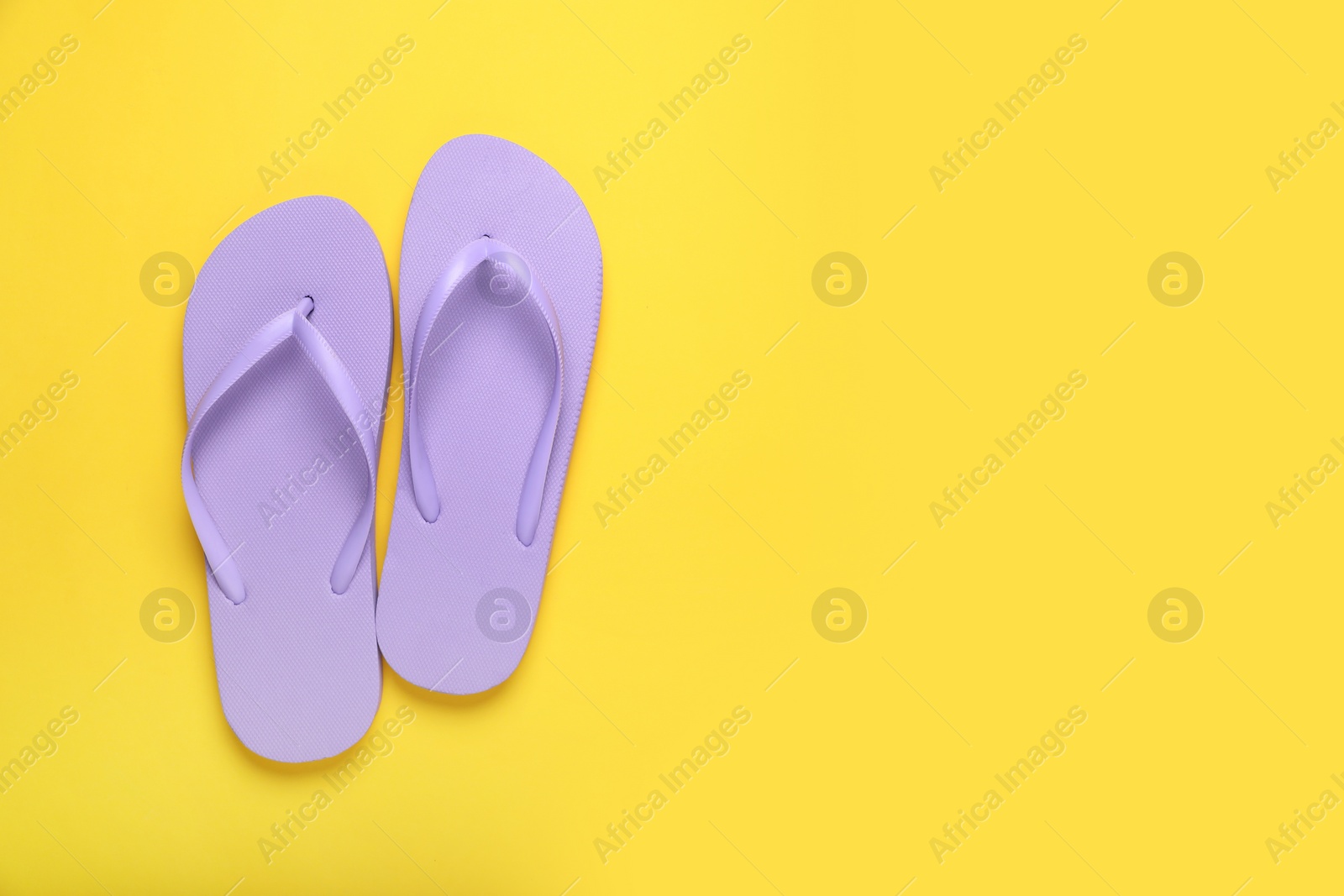 Photo of Stylish violet flip flops on yellow background, top view. Space for text