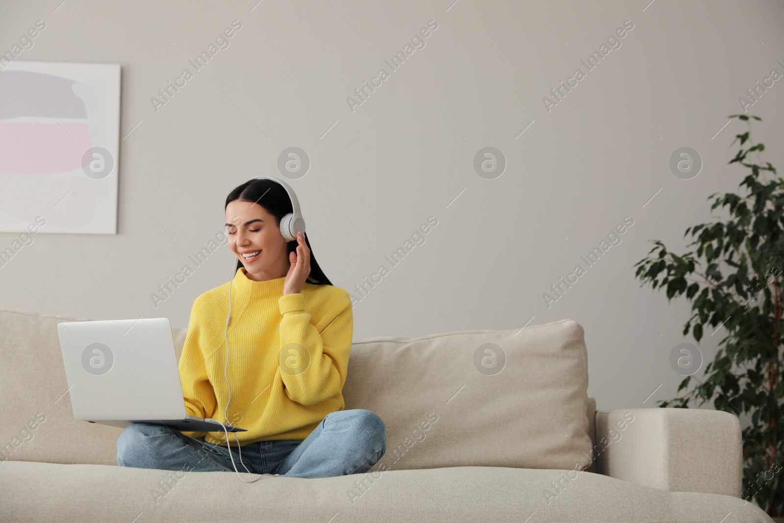 Photo of Woman with laptop and headphones sitting on sofa at home