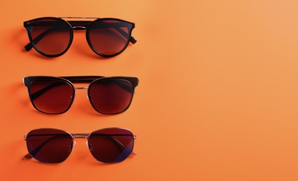 Many stylish sunglasses on orange background, flat lay. Space for text