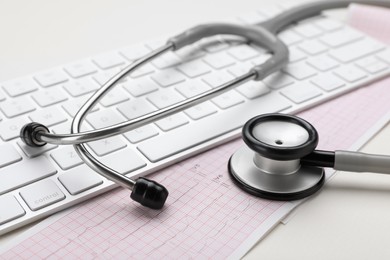 Photo of Keyboard, cardiogram paper and stethoscope on beige background, closeup