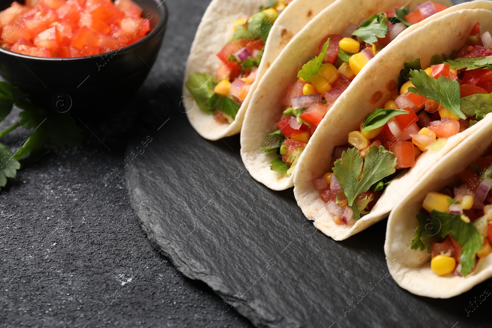 Photo of Tasty tacos with vegetables on black textured table, closeup. Space for text