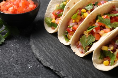 Tasty tacos with vegetables on black textured table, closeup. Space for text