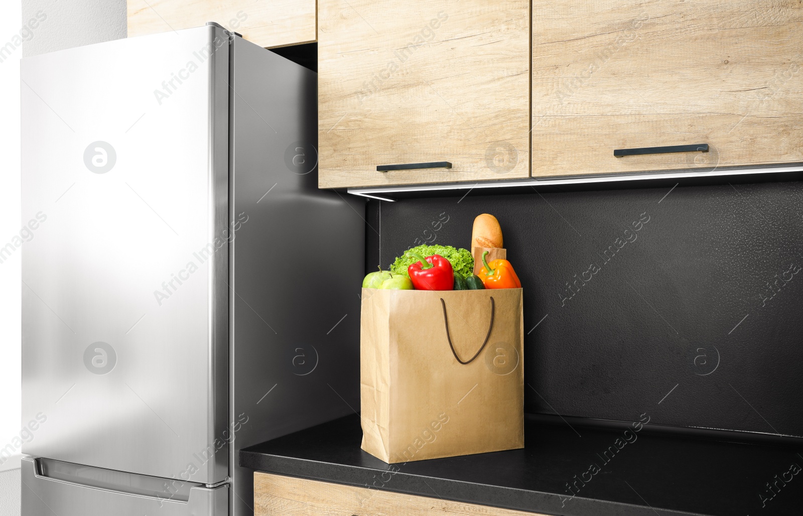 Photo of Paper bag with vegetables and other products on table in kitchen
