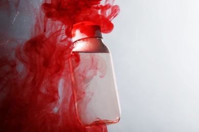 Photo of Bottlemicellar water in liquid with diffusing red paint on light grey background. Space for text