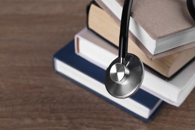 Stack of student textbooks and stethoscope on wooden table, closeup view with space for text. Medical education