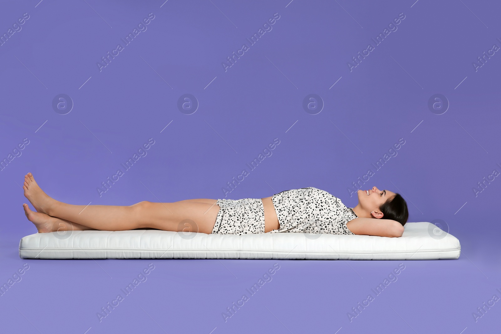 Photo of Young woman lying on soft mattress against light purple background